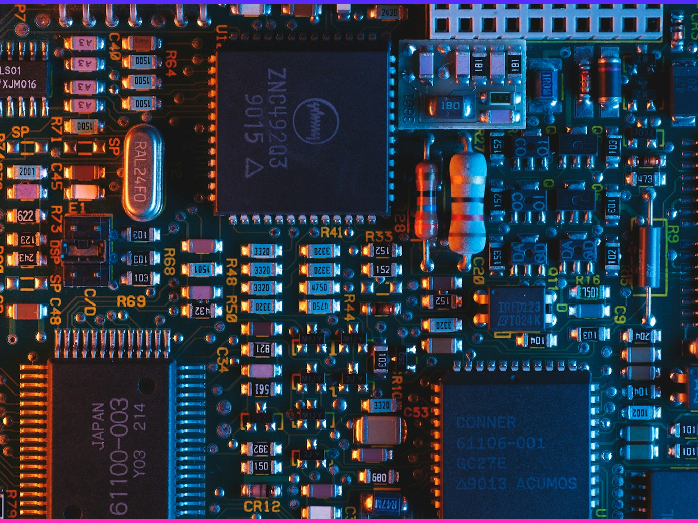 Macro shot of a circuit board's chips, resistors and solder joints lit in orange and blue